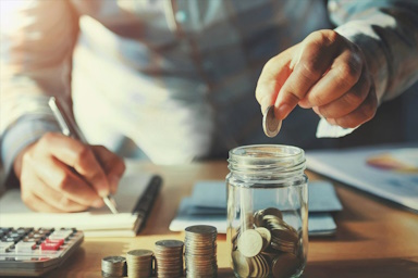 Man dropping coins into jar while budgeting